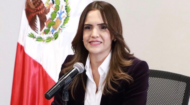 Clara Luz Flores ante un micrófono con la bandera de México al fondo; fotografía de archivo para análisis político de Nuevo León 2027.